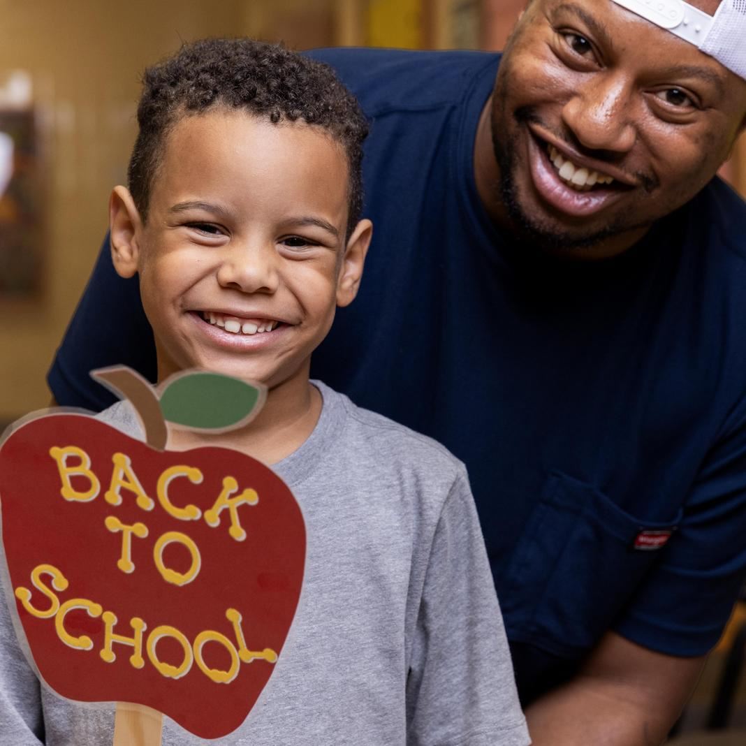  A parent and student smiling, the student holds a Back to School prop
